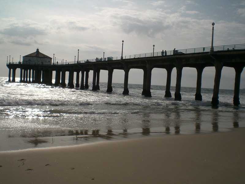 top: clouds and a gray-blue sky; middle a nearly-silhouetted pier and building, with sunlit breakers below; bottom: smooth, dull tan sand