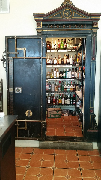 open black safe capped by a triangular pediment, inside (and on the inside of the door): alcohol bottles on shelves