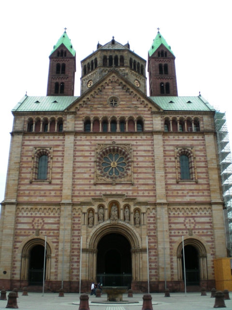 foreground: three-doored cathedral front with statues above center door; mid-ground: octagonal center tower; high background: flanking towers