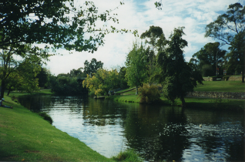 river from center to bottom right; grass bottom left; trees center and left; sky top center and right