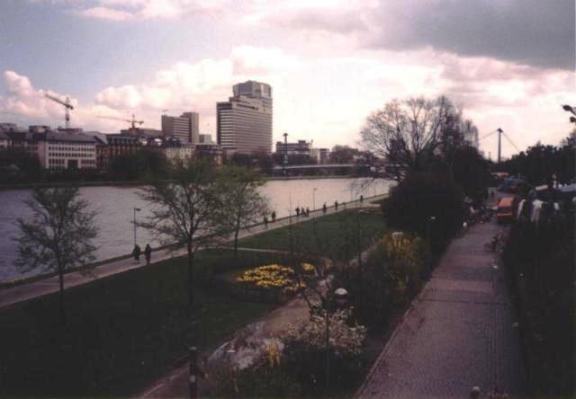 Main River, buildings on far side, garden park on near side, threatening clouds