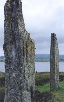 foreground: two stones on end, seen obliquely, in green meadow; water middleground; hills background